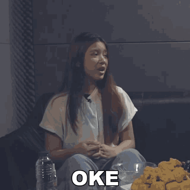 a woman sitting on a couch with a bowl of chicken nuggets and a sign that says oke on it