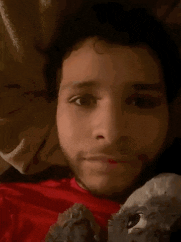a man in a red shirt is laying in bed holding a stuffed animal .
