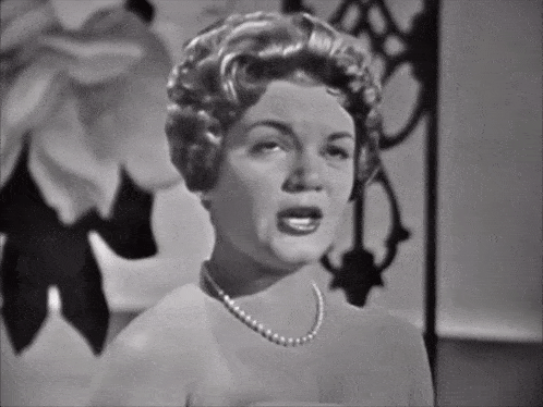 a woman wearing a pearl necklace is singing