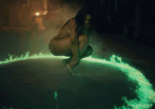 a woman in a bikini is squatting in front of a circle of green fire