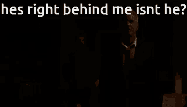 a man in a suit and tie is standing in the dark with the words he 's right behind me isn 't he