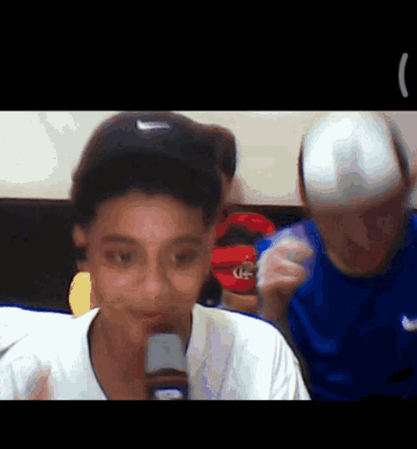 a boy wearing a nike hat is holding a microphone in his mouth