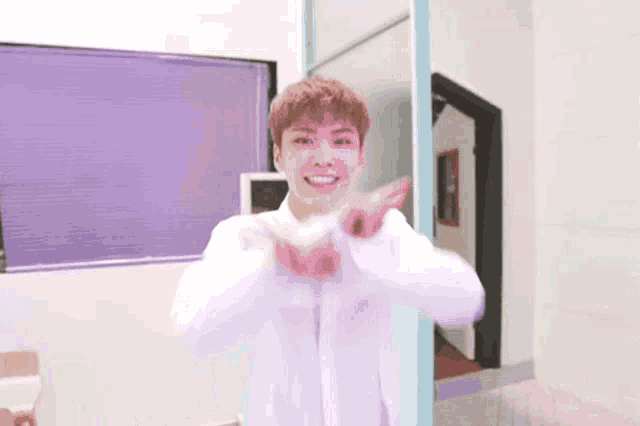 a young man in a white shirt is smiling and making a heart with his hands