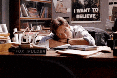 a man sits at a desk with a sign that says fox mulder on it