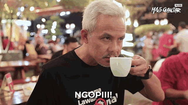 a man drinking a cup of coffee with a shirt that says ngopi !!!