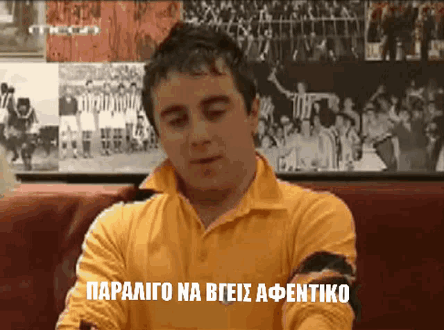 a man in a yellow shirt is sitting on a couch with the words paralio na bgeis afentiko written on the screen
