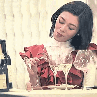 a woman is sitting at a table with a bottle of wine and glasses of wine .