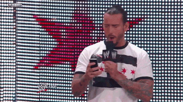 a man in a striped shirt holds a cell phone in front of a screen that says wwe live