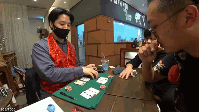 a man wearing a mask is playing a game of poker at a table in front of a sign that says stream now