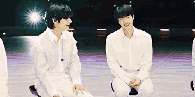 a group of young men in white shirts are sitting next to each other on a stage .