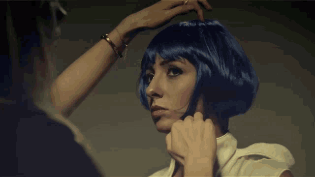 a woman wearing a blue wig looks at the camera