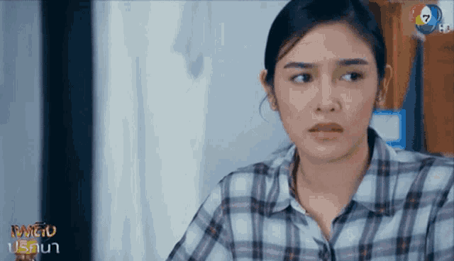 a woman in a plaid shirt is sitting in front of a tv screen that says ' thailand ' on it