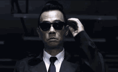 a man in a suit and tie is adjusting his sunglasses in a dark room .