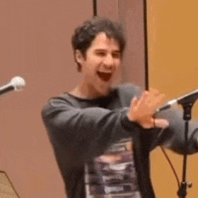 a man is standing in front of a microphone holding a stack of books and laughing .