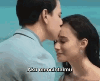 a man is kissing a woman on the forehead and the woman is saying aku mencintaimu .