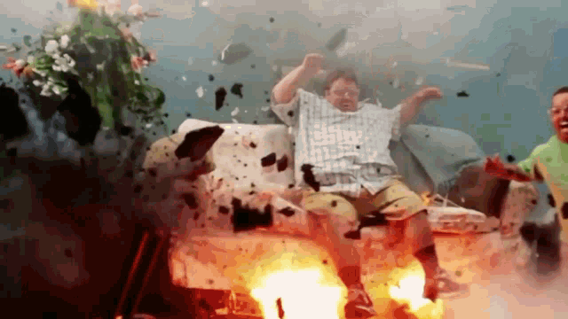 a man in a plaid shirt is sitting on a couch in front of an explosion
