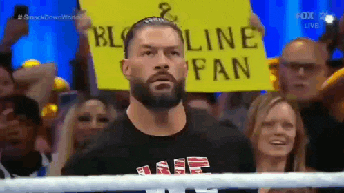 roman reigns is holding a sign in front of a crowd that says bloodline fan .