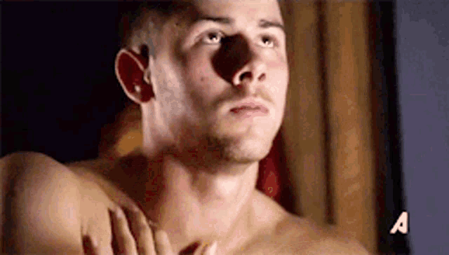 a shirtless man is standing in a dark room with a woman holding his chest .