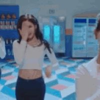 a woman in a crop top is covering her face with her hand while standing in a room .