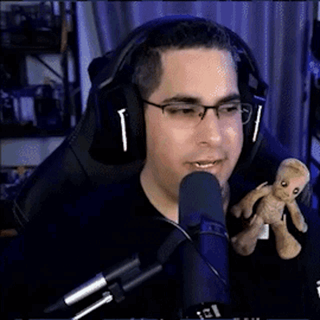 a man wearing headphones and glasses is holding a stuffed groot and talking into a microphone .