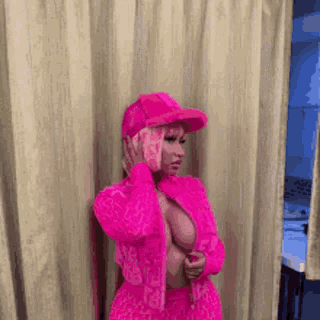 a woman in a pink jacket and hat is standing in front of a window .