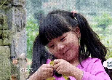 a little girl with pigtails and a pink shirt is smiling and holding a piece of paper .
