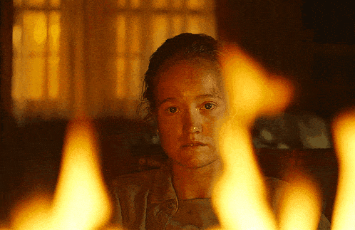 a woman is sitting in front of a fire and looking at the camera