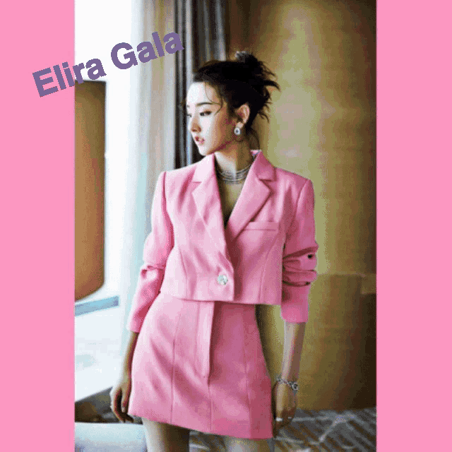 a woman in a pink suit is standing in front of a window with the name elira gala on the bottom