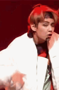 a young man wearing a white jacket and a red headband is dancing on a stage .