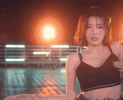 a woman in a black crop top stands in front of a fence with the letter e on it