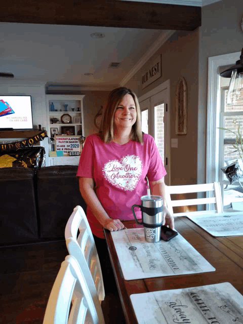 a woman wearing a pink shirt that says " i love one another " sits at a table