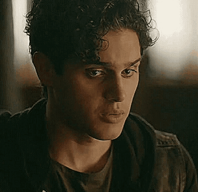 a close up of a man 's face with curly hair wearing a black jacket .