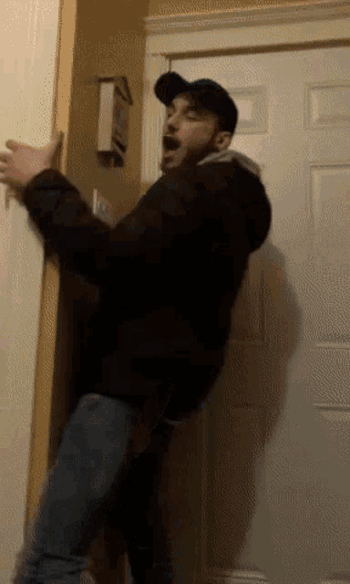 a man in a black jacket is standing in front of a door with his mouth open