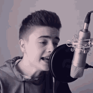 a young boy is singing into a microphone while wearing a grey hoodie .