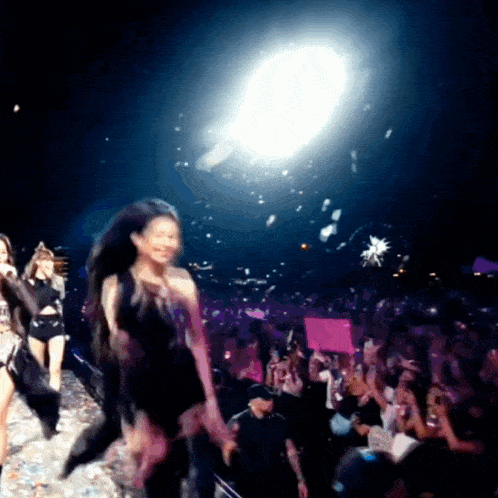 a woman in a black dress stands on a stage in front of a crowd