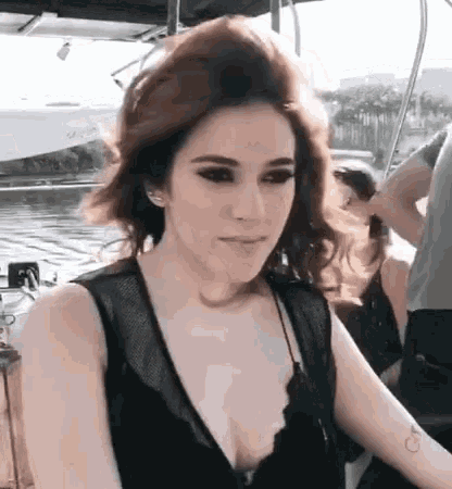 a woman in a black tank top is sitting on a boat looking at the camera .