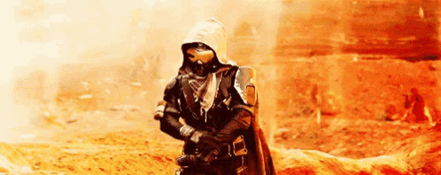 a man in a hooded cape is standing in the middle of a desert holding a gun .