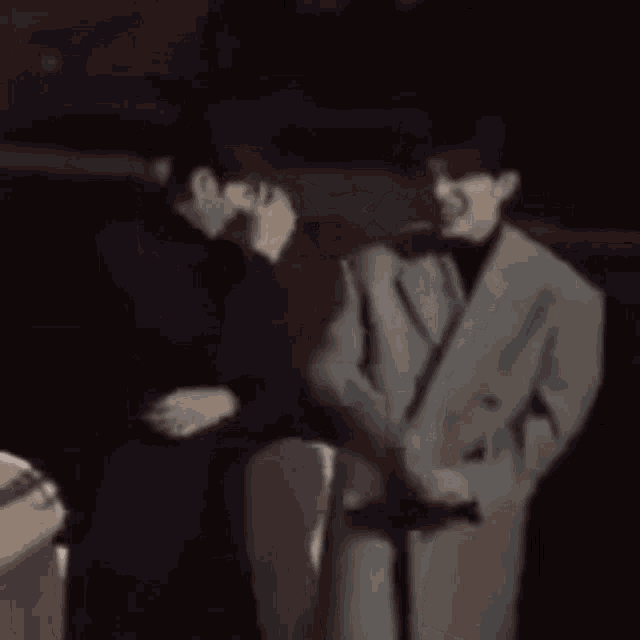 two men in suits are standing next to each other in a dark room and talking .