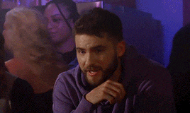 a man in a purple sweatshirt is sitting at a table with a woman behind him .
