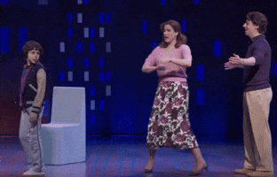 a woman in a floral skirt is dancing on stage with two men
