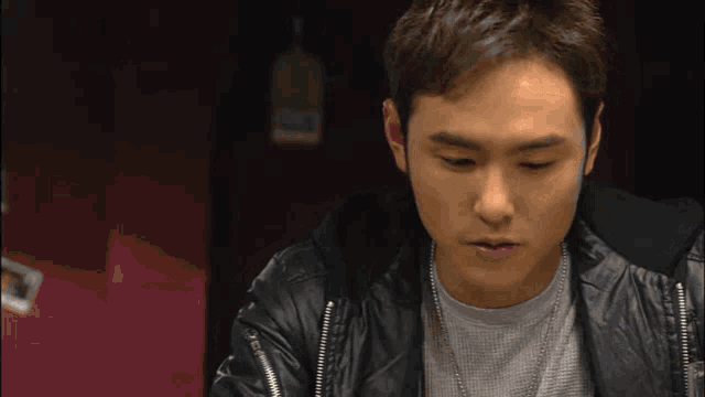 a man wearing a leather jacket and a necklace looks down at something