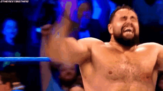 a shirtless man with a beard is standing in a wrestling ring with his arms in the air .