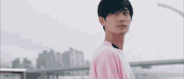 a young man in a pink shirt is standing in front of a bridge