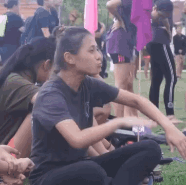 a woman is sitting on the grass with her legs crossed in front of a group of people .