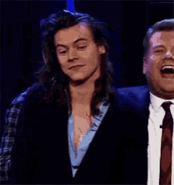 harry styles is standing next to a man in a suit and tie and laughing .