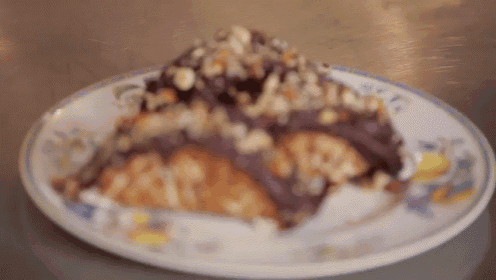 a white plate with a piece of cake on it with nuts on top