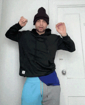 a man wearing a black hoodie and a beanie is standing in front of a white door