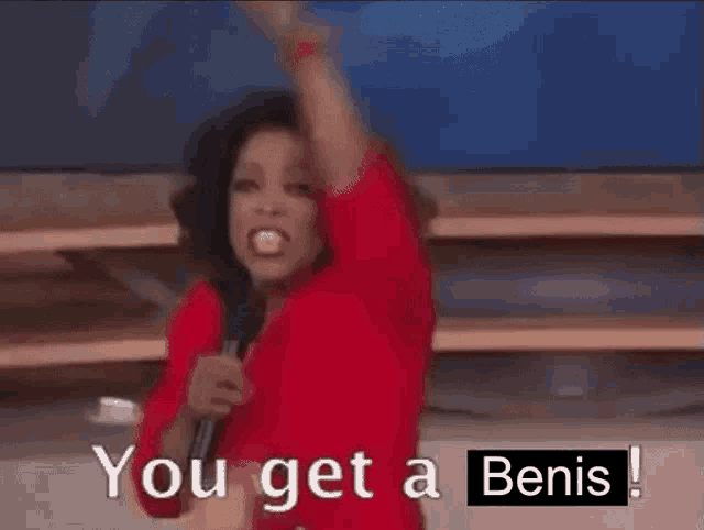a woman in a red shirt is holding a microphone and pointing at the camera while saying you get a benis !