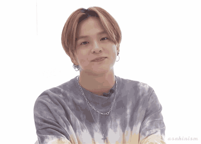 a young man wearing a tie dye sweater and a cross necklace looks at the camera