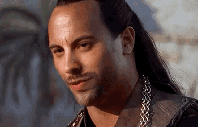 a man with long hair and a beard is wearing a leather jacket and a chain around his neck .